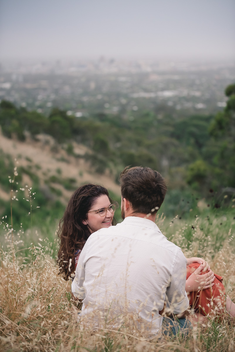 engaged couple sitting in grass before sunset