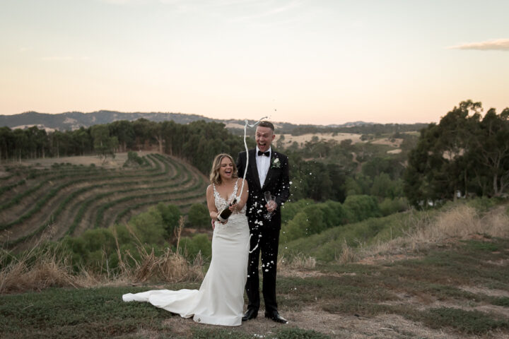 Married couple get the best from their wedding photographer popping champagne at sunset