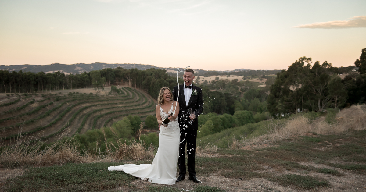 Married couple get the best from their wedding photographer popping champagne at sunset