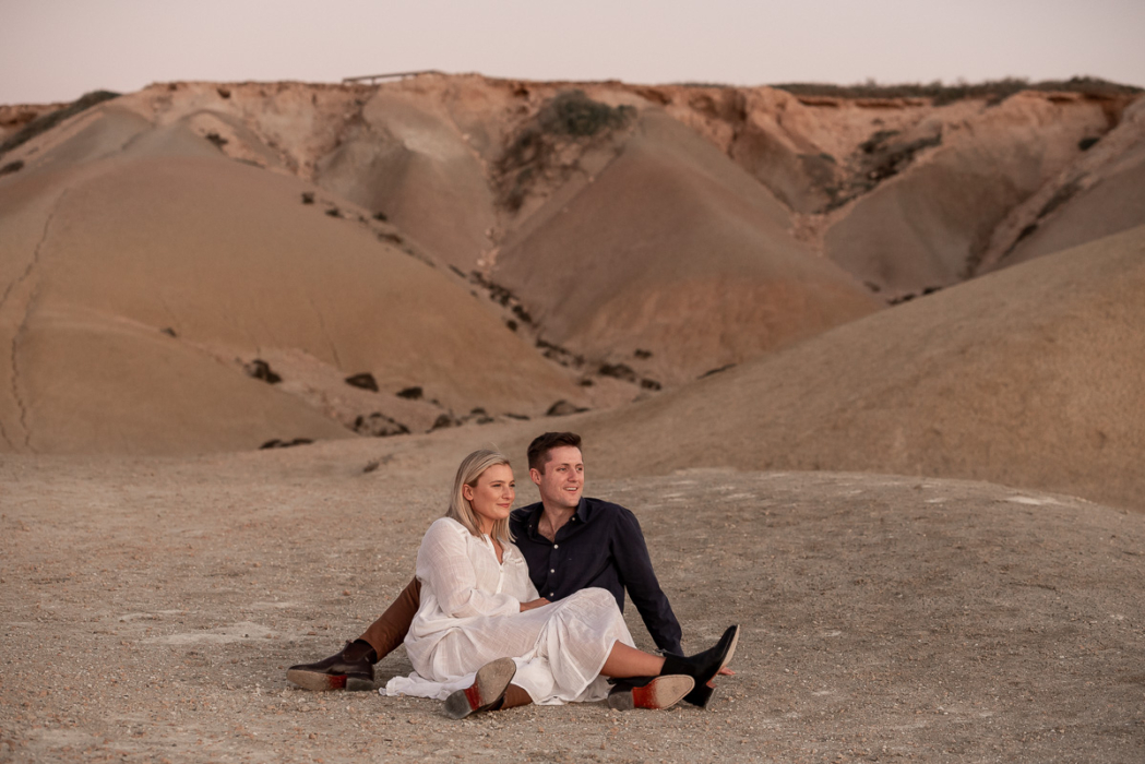 couple sitting near sand dunes - Adelaide Engagement Photography by Wilson & Lewis Photography